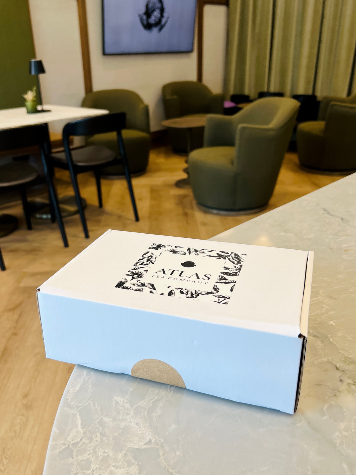 A closed white Comfort Box with the Atlas Tea Company illustration on the lid, on a counter in the Ogden tea shop.